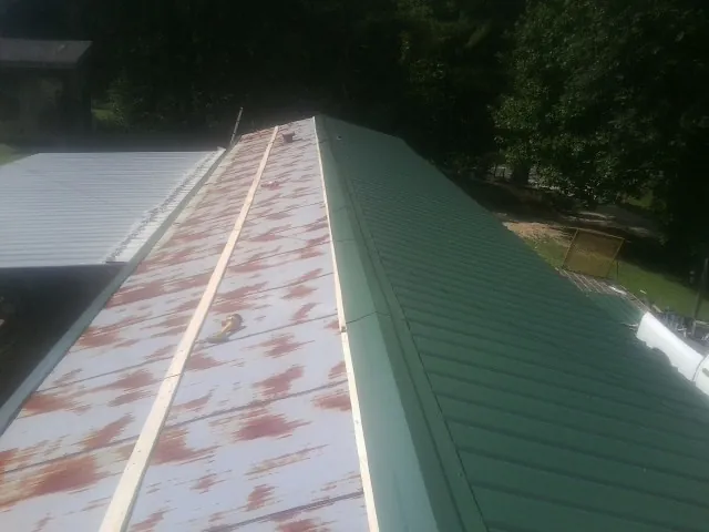 Old rusted panels beside newly installed green metal roofing — Wind Damage Roof Repair by Roofing Brothers in Eaton