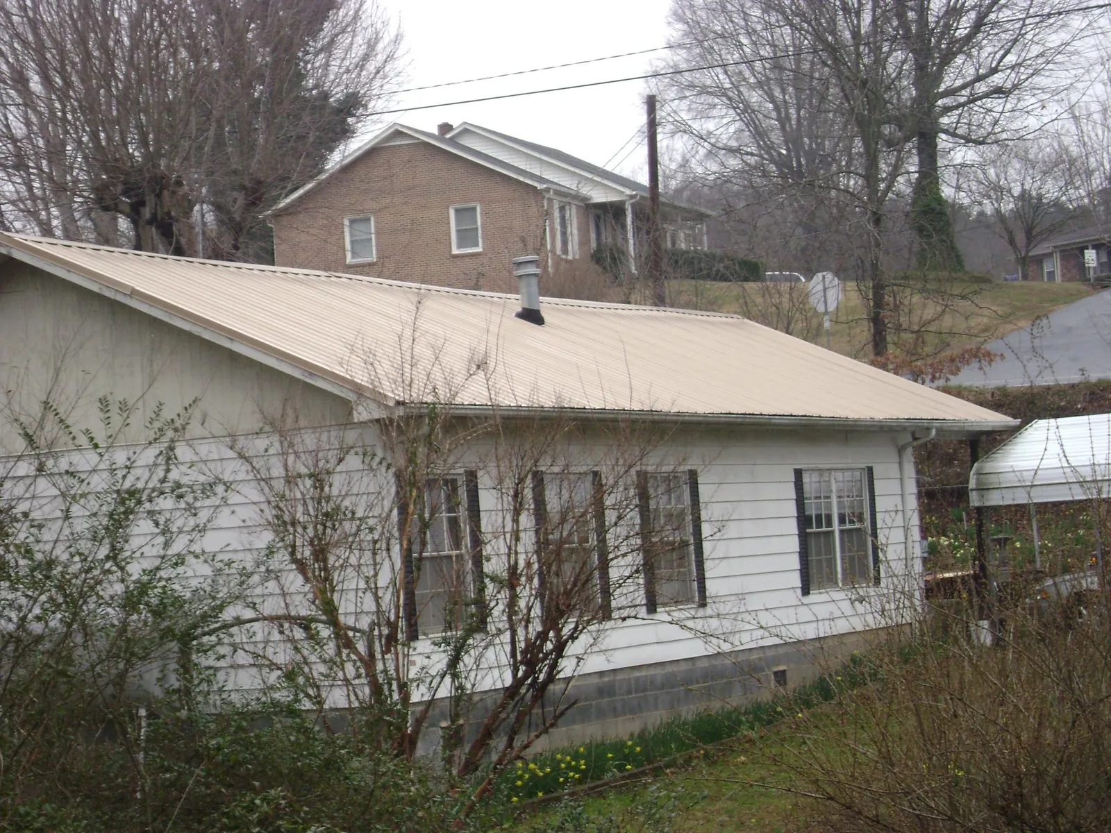 Tan metal roof on a white sided house set into a hillside — Commercial Roofing by Roofing Brothers in Eaton