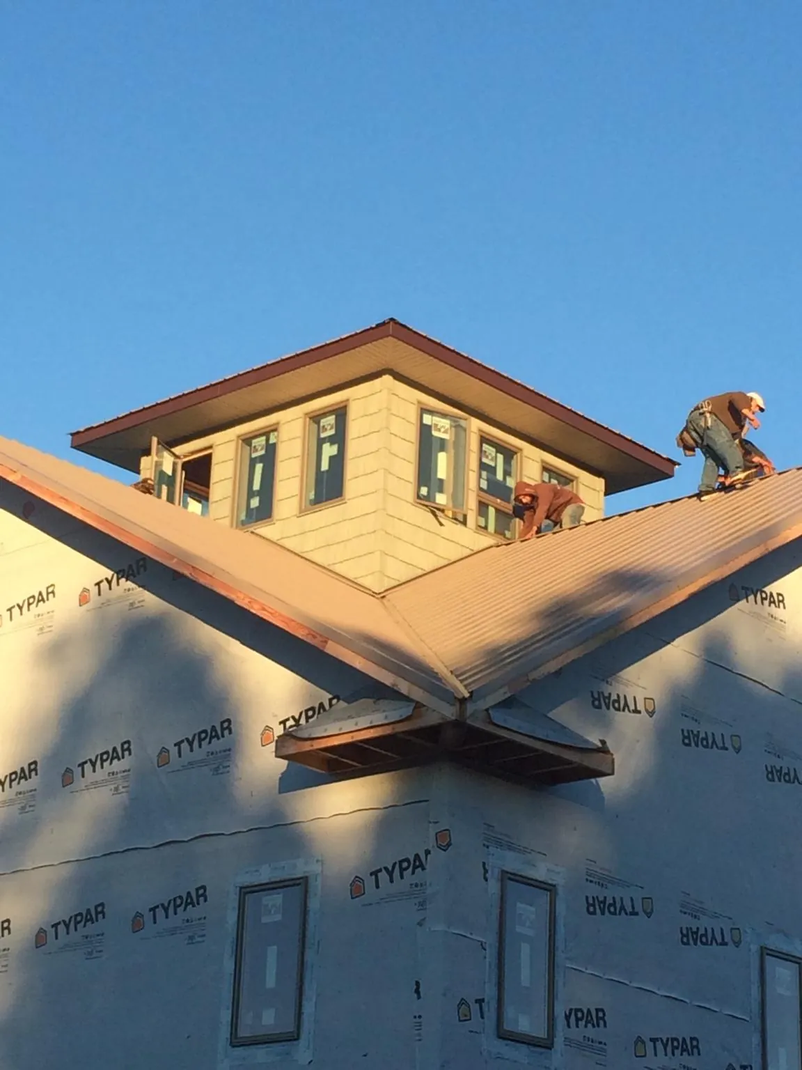 Roofers working around a rooftop cupola on a new metal roof at sunset in Eaton